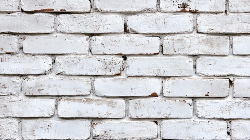 Close-up of a white-washed brick wall displaying a rustic, uneven white finish that preserves the natural texture and variations of the underlying red brick, visible through patches where the white coating is thinner