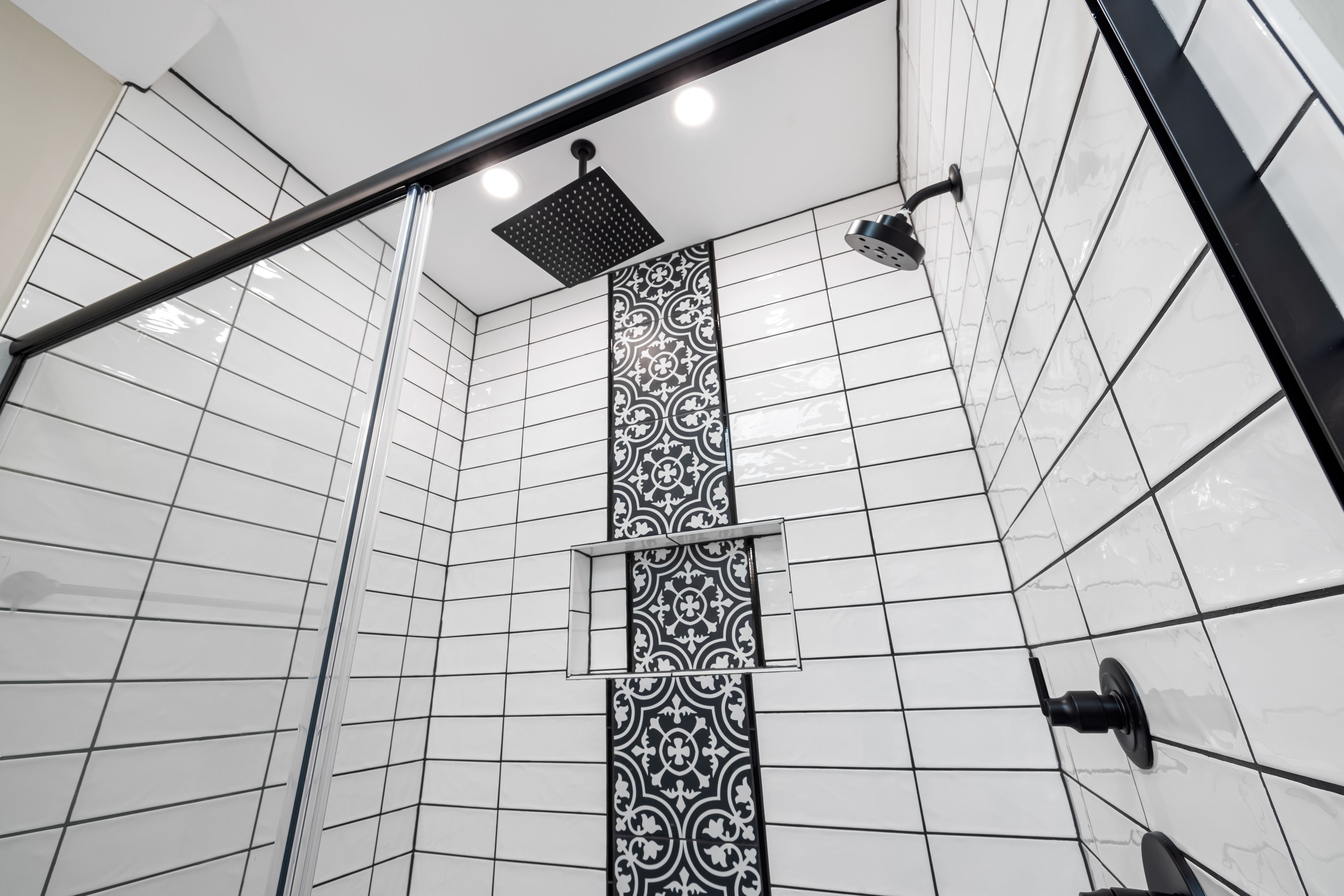 Modern bathroom with patterned tile, shower, and black fixtures after renovation.