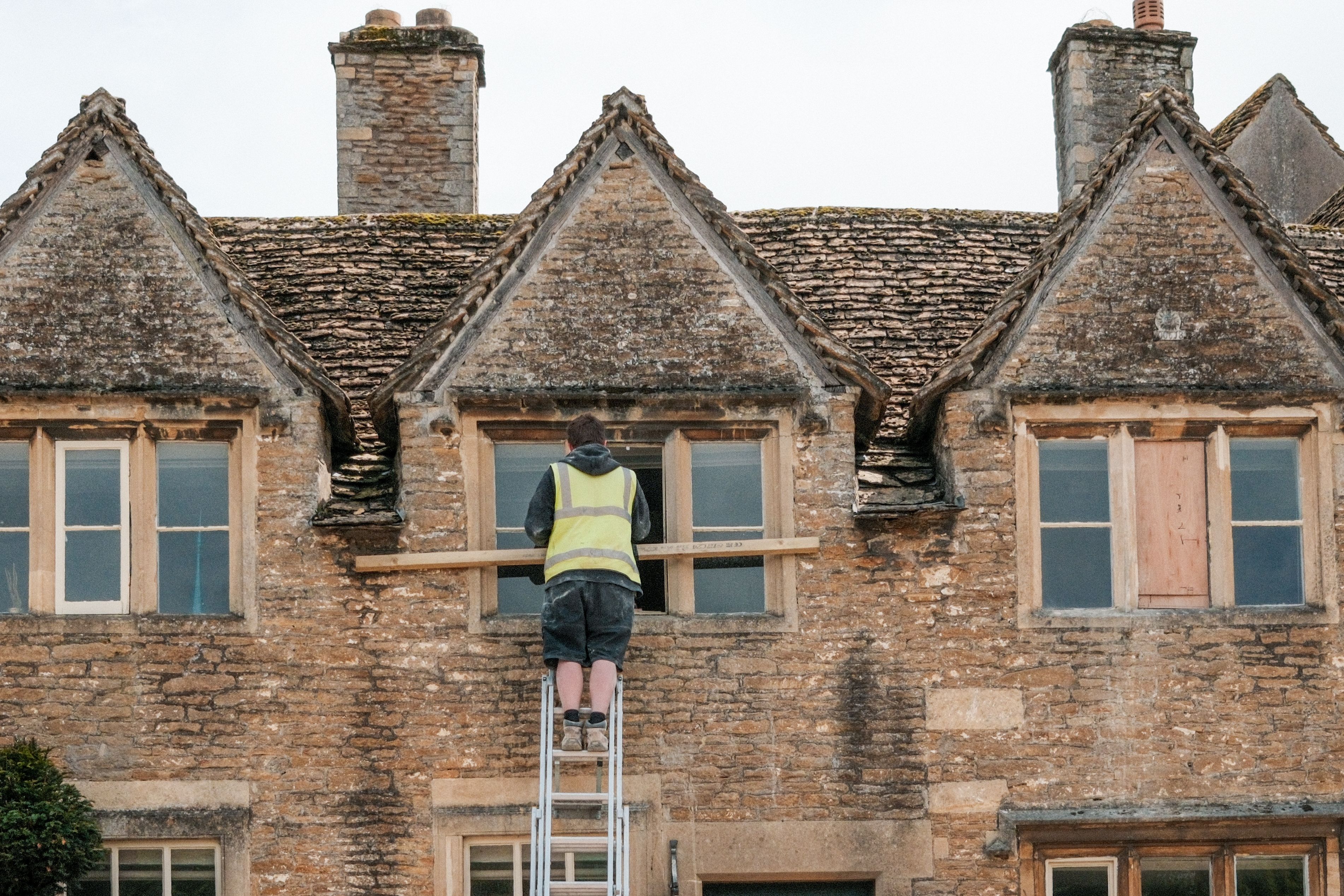 Construction worker repairing a window on a stone building, representing exterior maintenance for an older home.